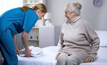 Nurse preparing clean bed-linen to elderly female patient in medical center